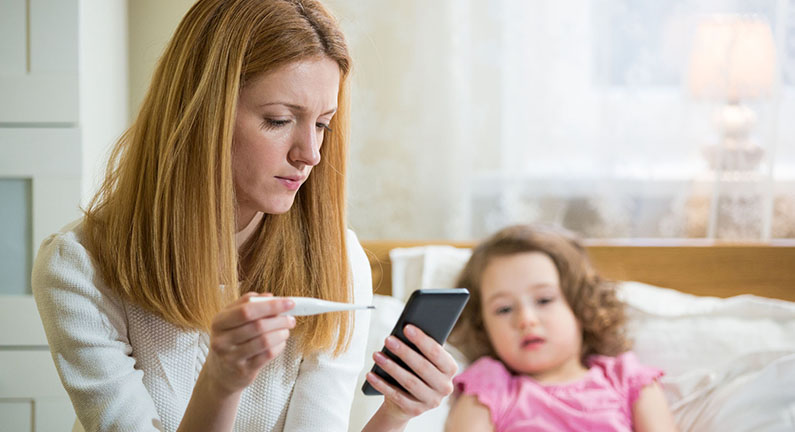 Mother measuring temperature of her ill kid. Sick child with high fever laying in bed and mother holding thermometer. Mother with cell phone calling to doctor