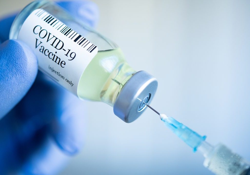 Doctor drawing up Covid-19 vaccine from glass phial bottle and filling syringe injection for vaccination. Close up of hand wearing protective disposable gloves in lab and holding a bottle of vaccination drugs. Hand with blue surgical gloves taking sars-coV-2 vaccine dose from vial with syringe: prevention and immunization concept.